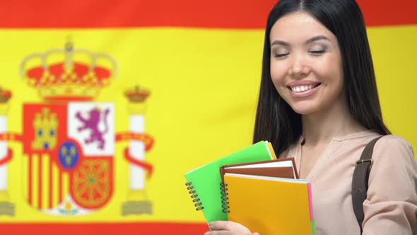 Woman With Notebooks Smiling Against Spanish Flag Background, Student Exchange