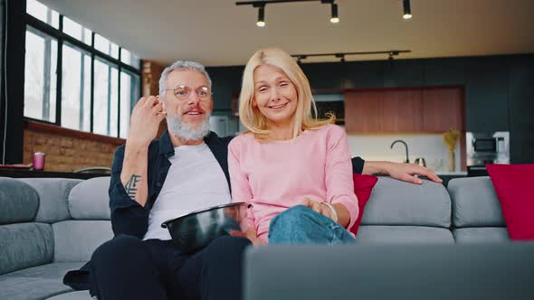 Husband and Wife on a Grey Corner Sofa with Red Cushions Watching Something Interesting on a Laptop