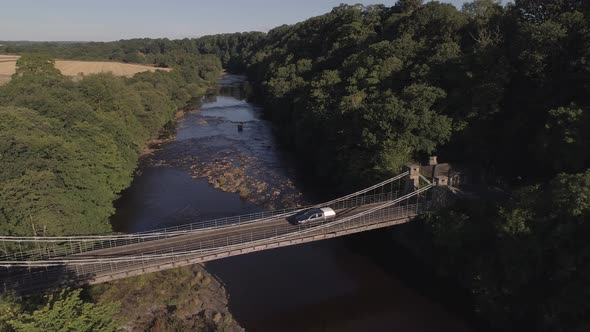 Utility vehicle crossing bridge over the river tees, in a slow aerial rise up shot above some trees