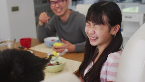 Happy asian father in kitchen eating breakfast with laughing son and daughter