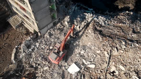 An Excavator Tractor Digs the Concrete Ruins of a Collapsed House with a Bucket