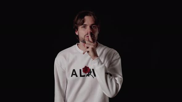 Trendy Young Man shushing into the camera, silence gesture, wide, black background