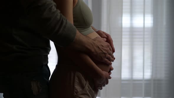 A man walks up to his pregnant wife and strokes her pregnant belly with her