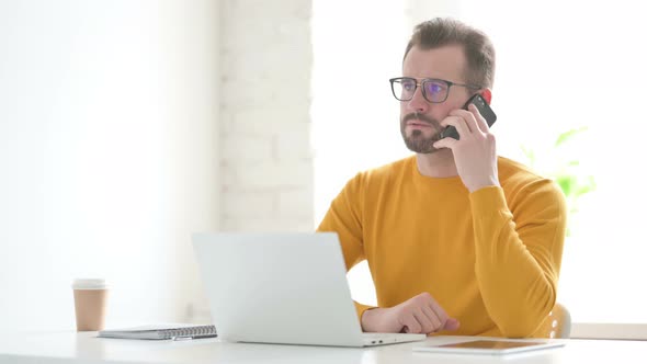 Man Talking on Phone While Using Laptop in Office