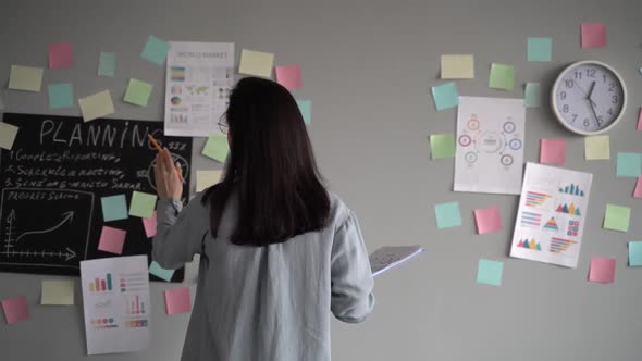 Young woman sticking notes on wall in office.