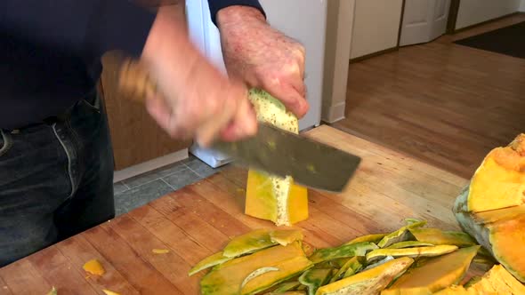 Man in home kitchen cutting a large pumpkin Blue Hubbard Squash with a Chinese cleaver