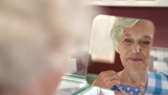 Mature Lady Looking at Mirror While Trying on Pearl Necklace