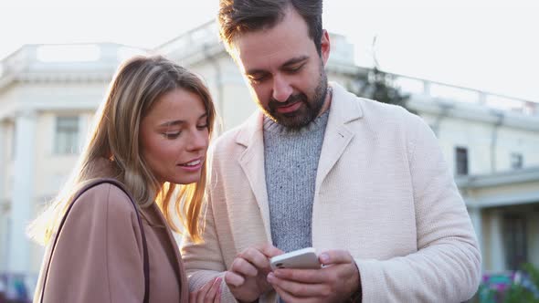 Positive couple looking at the phone and pointing in different directions