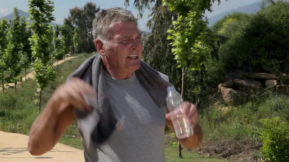 Senior male jogger wiping face with towel and having a drink of water
