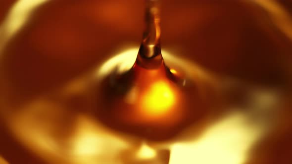 Super Slow Motion Shot of Droplet Falling Into Golden Liquid at 1000Fps.