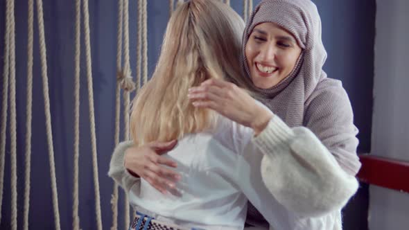 Muslim and Western Female Friends Are Meeting in Cafe, Embracing and Rejoicing