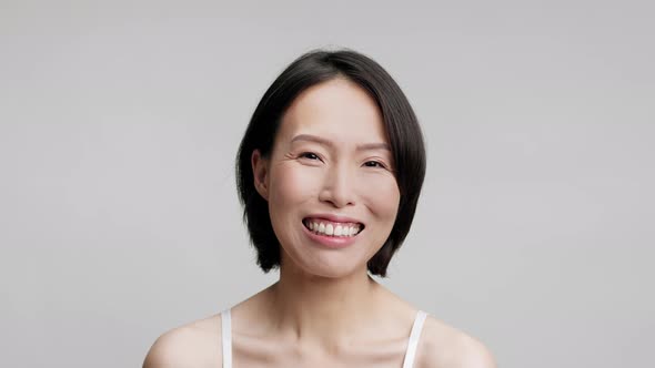 Mature Asian Woman Posing Smiling To Camera Over Gray Background