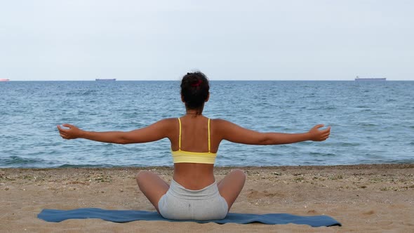 Beautiful tanned young woman sitting in a meditation pose on the beach. Goods for health.