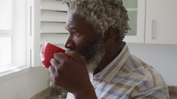 Senior man drinking coffee while looking out of window in kitchen