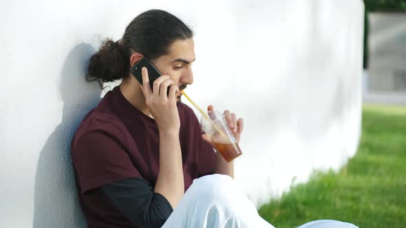 Portrait of Young Attractive Arab Man Sitting on the Grass and Talking on the Phone