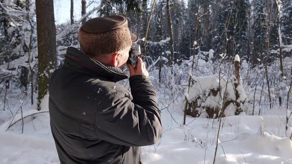 Old Man is Photographing Nature in Snowy Winter Forest at Sunny Weather Photographer is Taking
