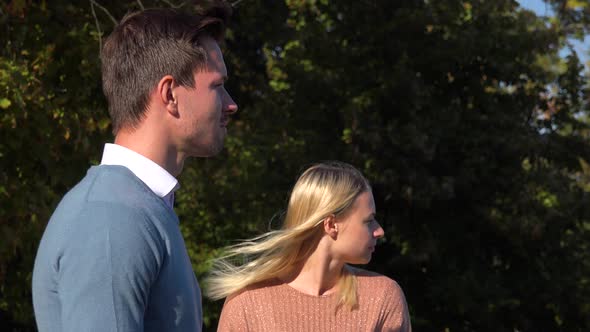 A Man and a Woman Stand in a Park and Look Into Distance