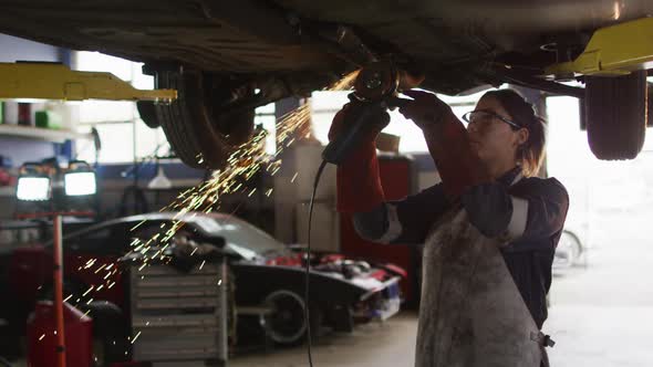 Female mechanic using electric blade cutter and working under a car at a car service station