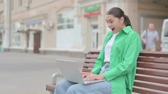 Hispanic Woman Celebrating Success on Laptop While Sitting Outdoor on Bench