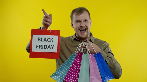 Man Showing Black Friday Inscription on Shopping Bags, Smiling, Satisfied with Low Prices Purchases