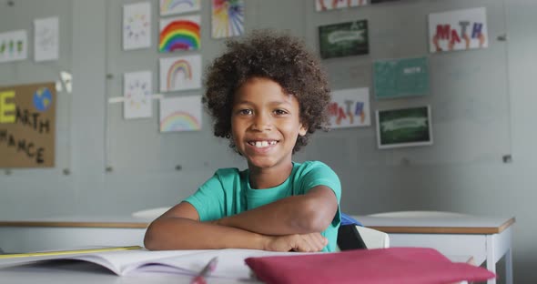 Video of happy biracial boy sitting at desk in classsroom alt