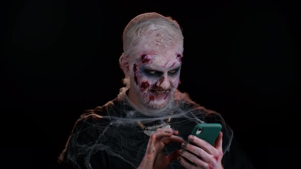 Frightening Man Halloween Zombie Using Mobile Phone Typing New Post on Web Browsing Addiction