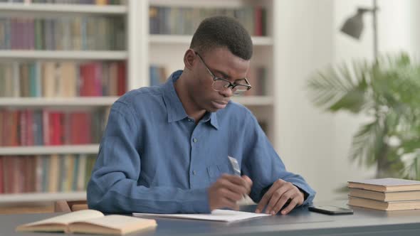 Young African Man Writing on Paper in Office