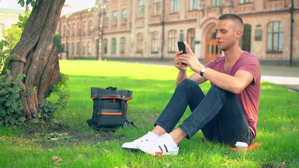 Young Man Sits Near the Tree Messaging Sms