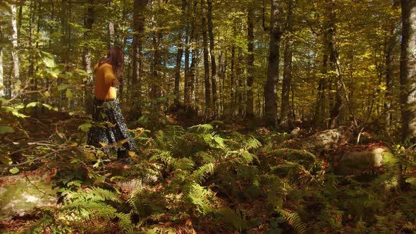 Girl is Carefully Stepping on Dry Tree Trunk Lying Among the Dence Vegetation in the Autumn Forest