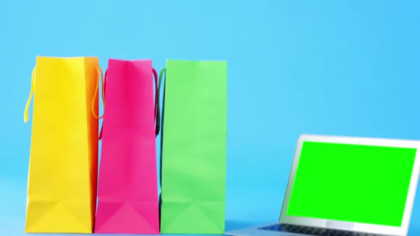 Multicolored shopping bags and laptop on blue background