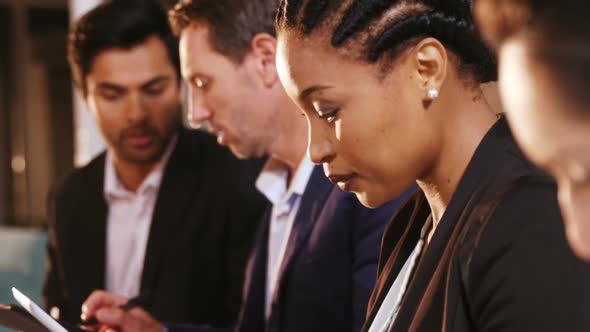 Businesswoman using digital tablet while colleagues writing notes