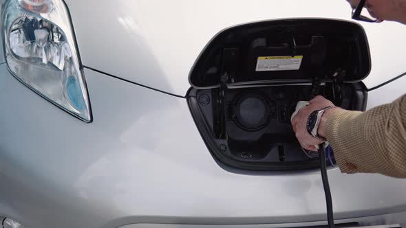 Senior Man Disconnects Charging Cable to Electric Vehicle