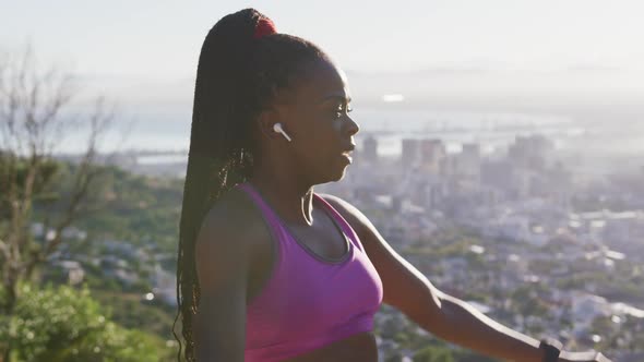 African american woman wearing wireless earphones stretching her arms outdoors