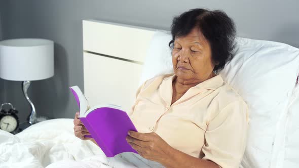 old woman reading a book on bed in bedroom