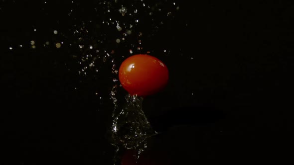 Red cherry tomato falling on a wet surface alt