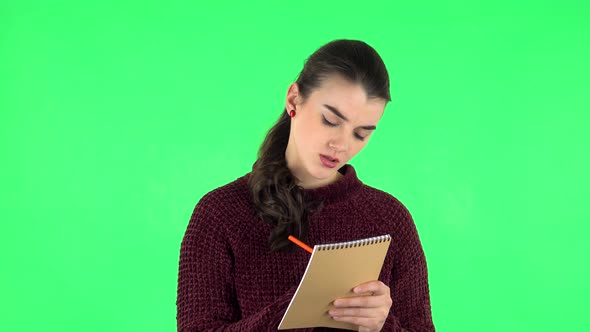 Girl Stands and Thinks, Then Angrily Writes with Pencil in Notebook. Green Screen