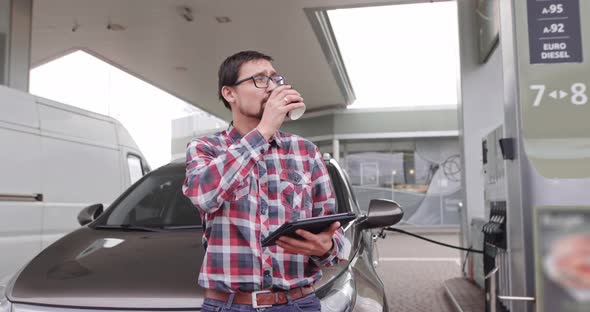 Handsome Young Caucasian Man at Petrol Station Standing Near the Car with Take