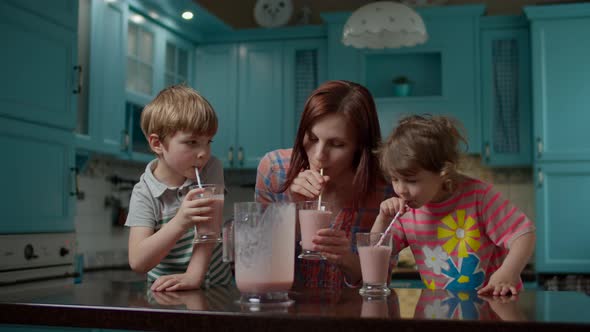 Happy family of mother and two kids drinking berry smoothie at home kitchen