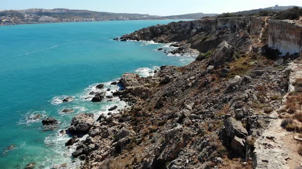 Aerial forward view of rocky cliffs, coast and blue sea in Mellieha bay, Malta