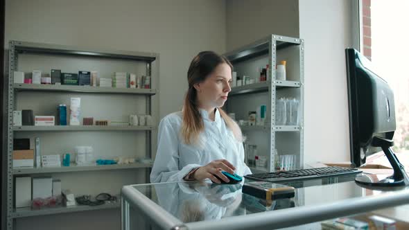 Young Saleswoman Looks at the Camera in the Interior of the Pharmacy