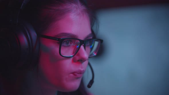 Young Attractive Woman in Glasses Playing Games in Modern Neon Gaming Club and Chewing a Bubble Gum