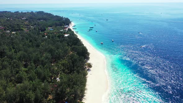 Blue azure sea surface reflecting sunlight of sunny summer day, white beach alongside green vegetati