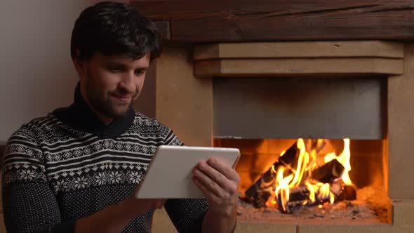 Man Using a Digital Tablet Sits By the Fireplace