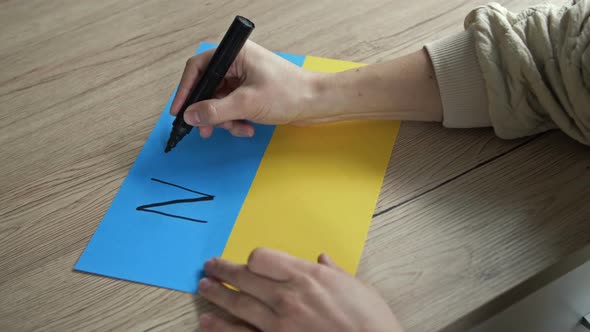 Woman's Hand Writes on the Background of the Ukrainian Flag NO WAR