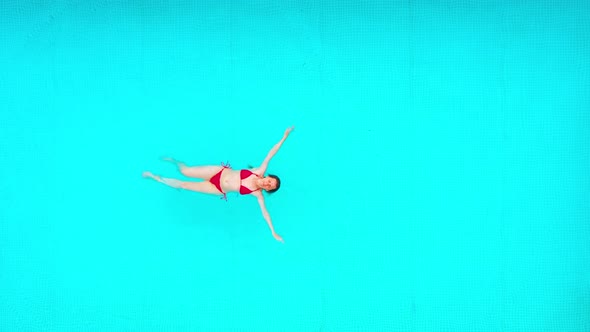 View From the Top As a Woman in Red Swimsuit Swims on Her Back in the Pool