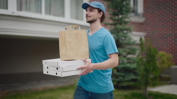 A Young and Energetic Delivery Man Carrying a Pizza and a Bag of Groceries