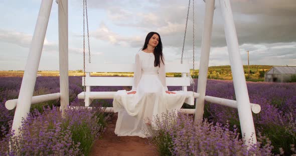 a Gentle Girl in a White Light Dress Swings on a Swing in a Field with Flowers