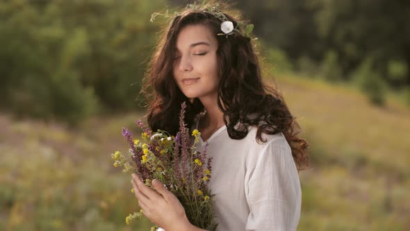 Natural Beauty Girl with Bouquet of Flowers Outdoor in Freedom Enjoyment Concept. Focus on Flowers