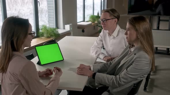 Three aspiring entrepreneurs are discussing a project with a green mockup screen on a tablet