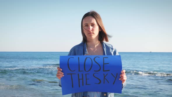 Upset ukrainian female holding blue banner with inscription Close The Sky